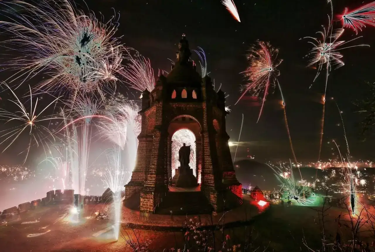 Spektakul&auml;res Feuerwerk erhellt den Himmel &uuml;ber Minden. Ein Denkmal steht im Zentrum, umgeben von bunten Raketen und Lichtern.