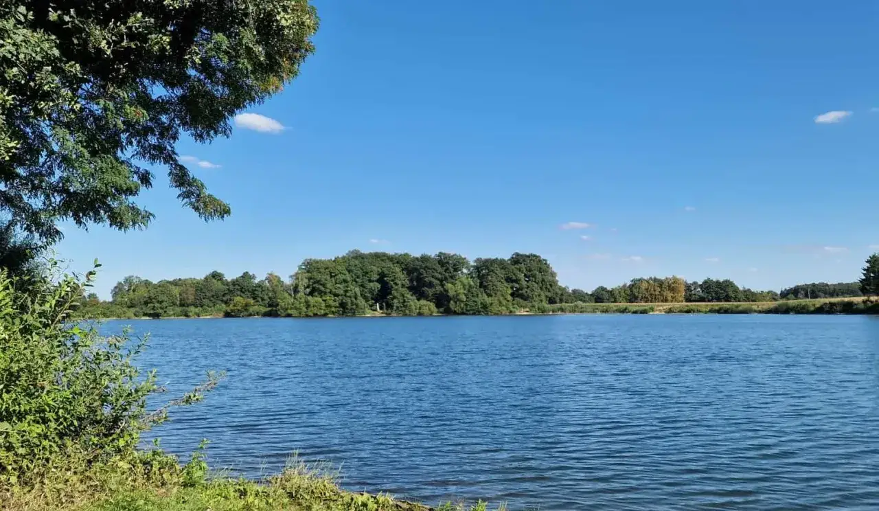 Blauer Himmel über dem ruhigen Linteler See, umgeben von üppigem Grün.