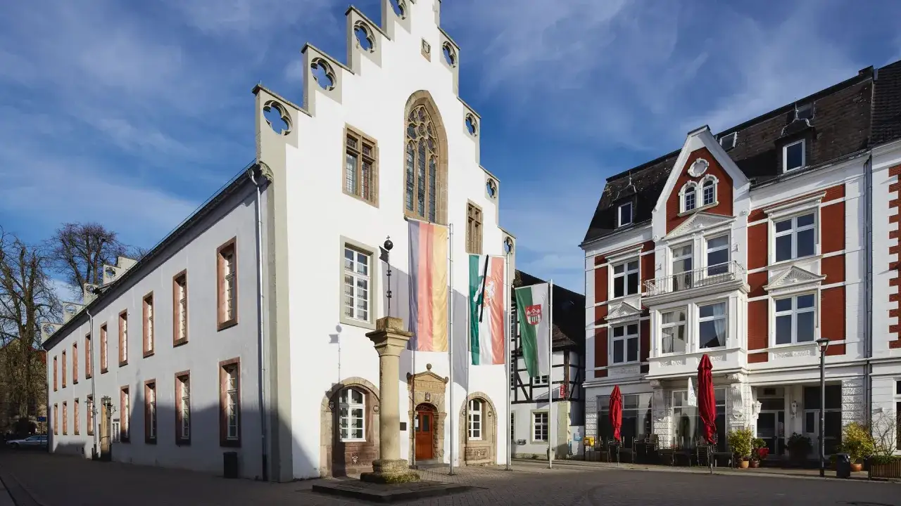 Der Markt in Brakel zeigt ein historisches Rathaus mit deutschen und regionalen Fahnen, daneben ein rotes Backsteingebäude mit Café.