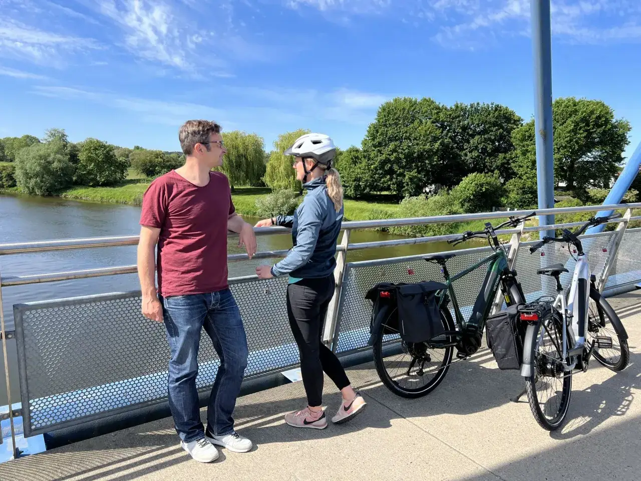 Ein Paar pausiert auf einer Br&uuml;cke w&auml;hrend einer Weser-Radweg Rundtour. Zwei Fahrr&auml;der stehen bereit f&uuml;r die Weiterfahrt.
