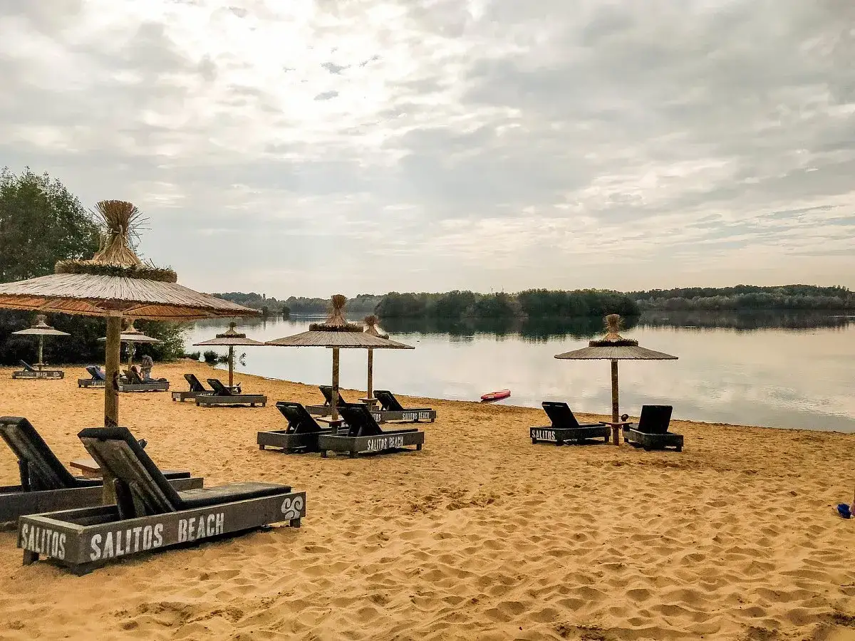 Sonnenliegen und Strohschirme am Sandstrand des Lippesee rundweg laden zum Entspannen ein. Ein ruhiger See und bewaldete Ufer im Hintergrund.