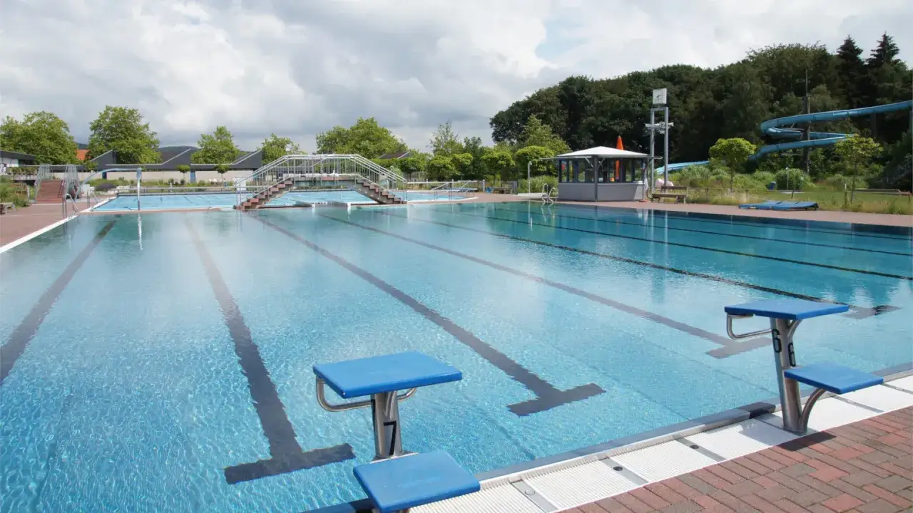 Das Freibad Porta Westfalica mit seinen blauen Sprungbl&ouml;cken und Bahnen l&auml;dt zum Schwimmen ein. Im Hintergrund eine Wasserrutsche.
