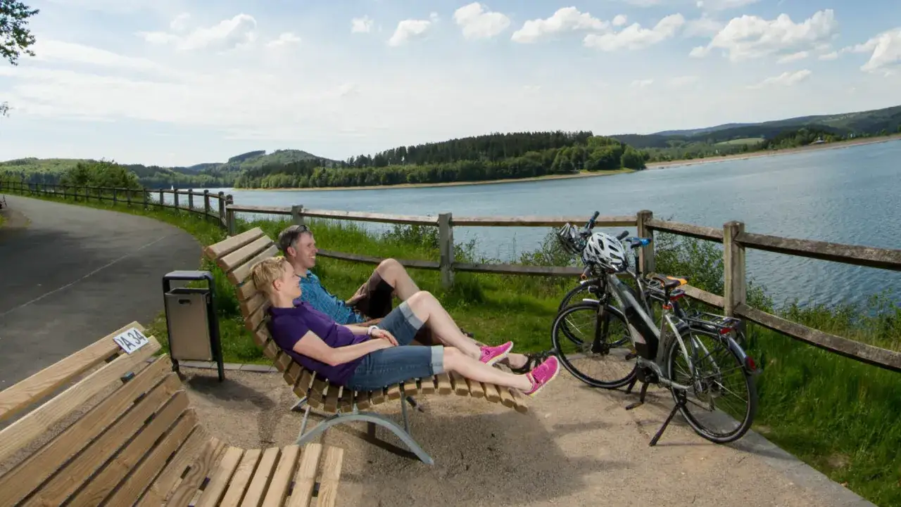 Ein Paar entspannt sich nach einer Sauertal Fahrradtour am See. Fahrräder stehen bereit.