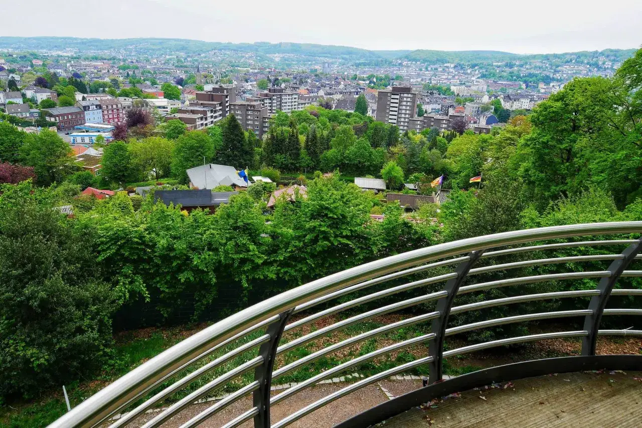 Blick über den grünen Nordpark Wuppertal mit Häusern und Bäumen. Im Hintergrund die Stadt und Hügel.