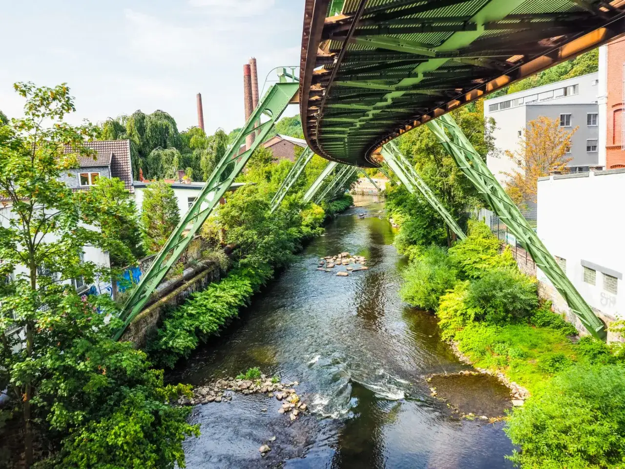 Schwebende Bahn &uuml;ber Fluss, gr&uuml;ne Ufer und alte Fabrikschlote. Ein toller Fotospot in NRW f&uuml;r einzigartige Perspektiven.