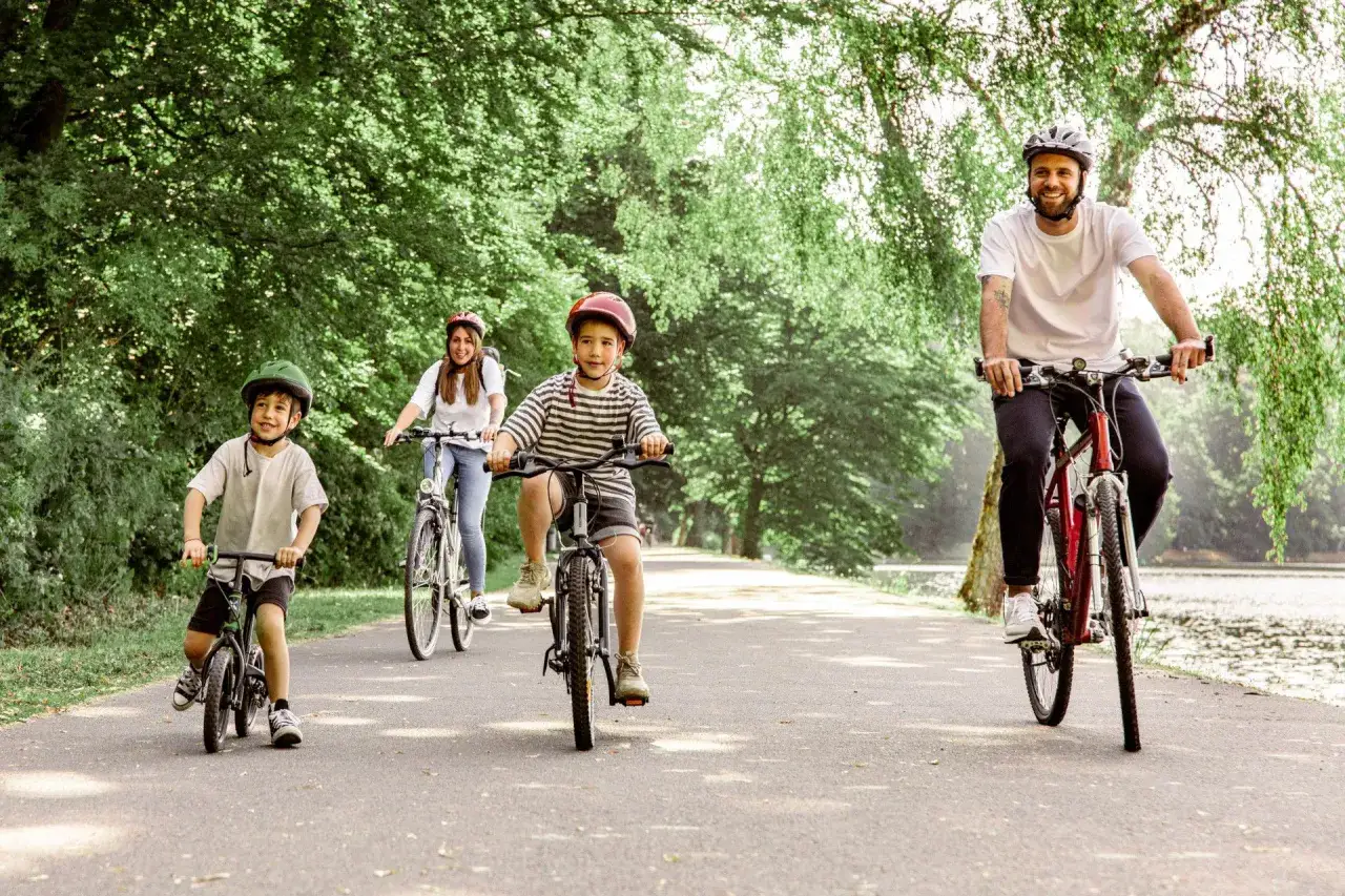 Familie genießt eine Fahrradtour mit Kindern in NRW. Vater, Mutter und zwei Jungen radeln auf einem asphaltierten Weg durch eine grüne Allee.