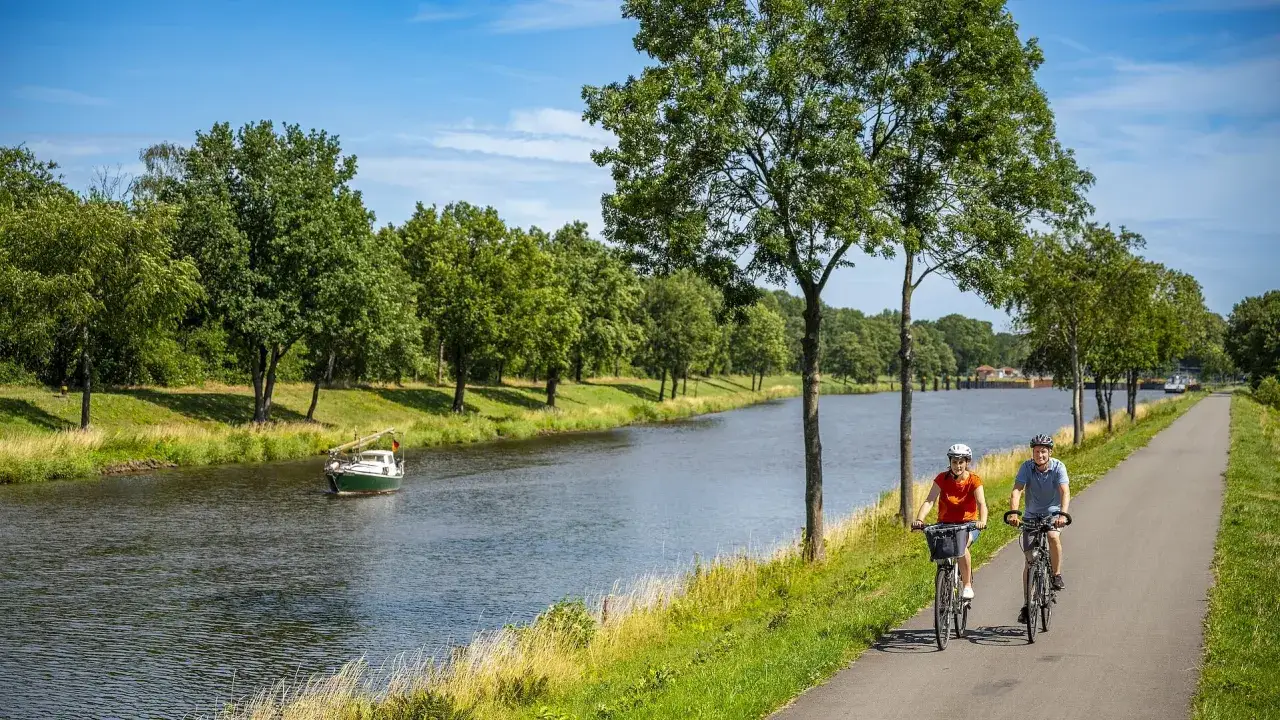 Zwei Radfahrer genießen die Fahrt auf dem Dortmund-Ems-Kanal-Radweg. Ein kleines Boot gleitet auf dem Wasser.