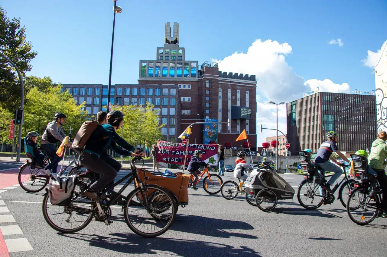Fahrradfahrer, darunter Kinder, nehmen an der Kidical Mass Dortmund teil. Sie fahren an Gebäuden vorbei, auf denen