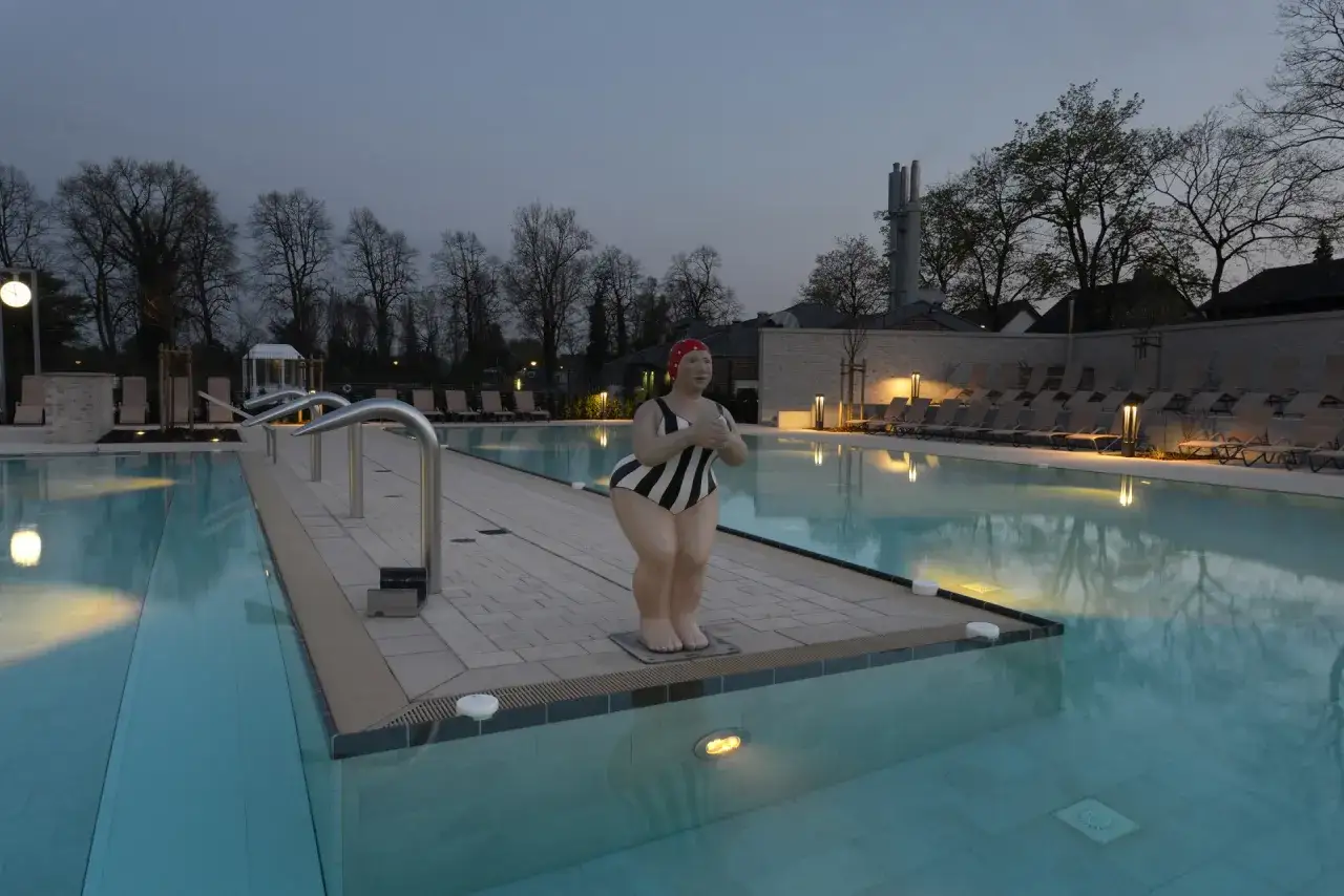 Skulptur einer Schwimmerin am Beckenrand des Solebad Werne. Liegen und B&auml;ume im Abendlicht.