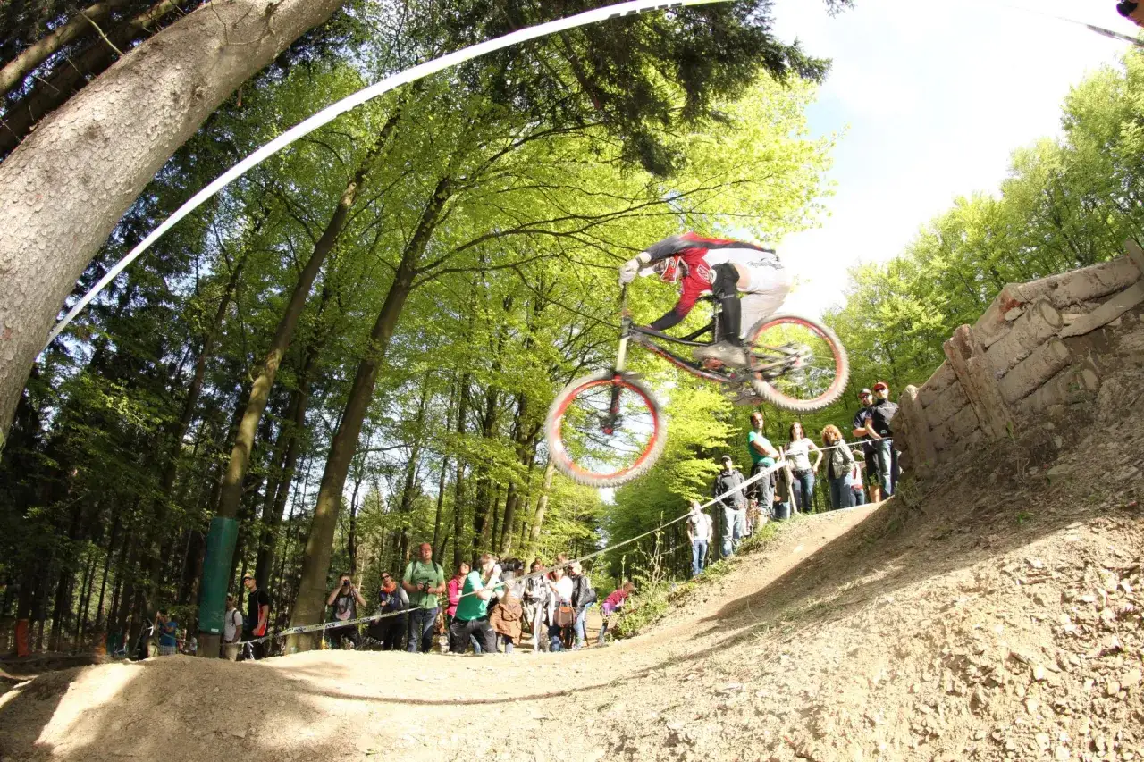 Downhill-Biker springt &uuml;ber eine Schanze bei den Dirt Masters Winterberg. Zuschauer feuern ihn an.