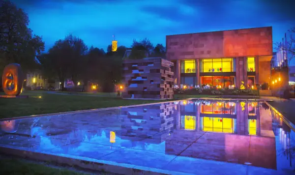 Abendstimmung am Museum mit reflektierendem Wasserbecken. Ein Turm leuchtet in der Ferne. Entdecke Bielefeld Geheimtipps!