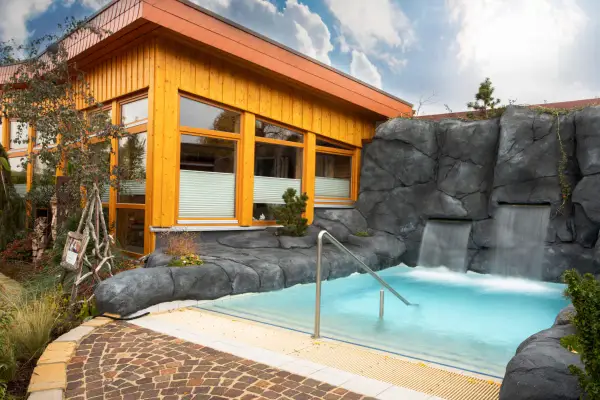 Entspannendes Wasserbecken mit Wasserfällen vor einer Holzhütte, ideal für eine H2O Sauna.