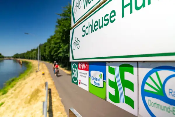 Radwegweiser am Schleusenweg zeigen den Verlauf des Emsland-Radwegs. Radfahrer genießen die Fahrt entlang des Kanals.