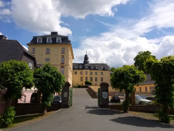 Schloss Wittgenstein in Bad Laasphe, ein gelbes Barockschloss mit Turm, umgeben von Bäumen und einem blauen Himmel mit Wolken.