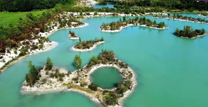Eine malerische **blaue Lagune** mit kleinen Inseln, bewachsen mit Bäumen und Sträuchern, umgeben von weißem Sand und grünen Hügeln.