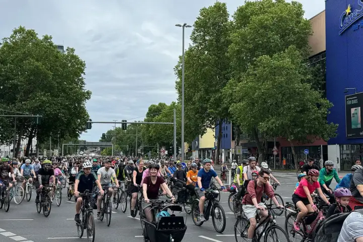 Große Gruppe Radfahrer bei der ADFC Sternfahrt. Viele Menschen auf Fahrrädern fahren auf einer Straße, umgeben von Bäumen und Gebäuden.