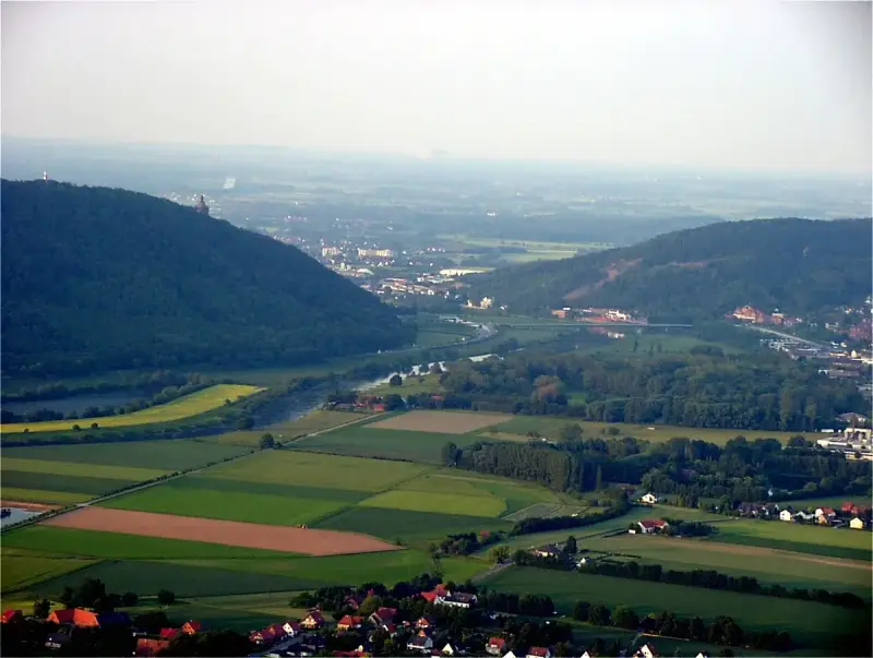 Blick über das Wesertal bei Porta Westfalica mit bewaldeten Hügeln, Feldern und der Stadt.