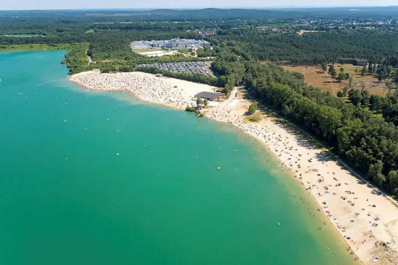 Sonniger Tag am **Silbersee Haltern am See**. Tausende Besucher genießen das türkisfarbene Wasser und den breiten Sandstrand, umgeben von grünen Wäldern.