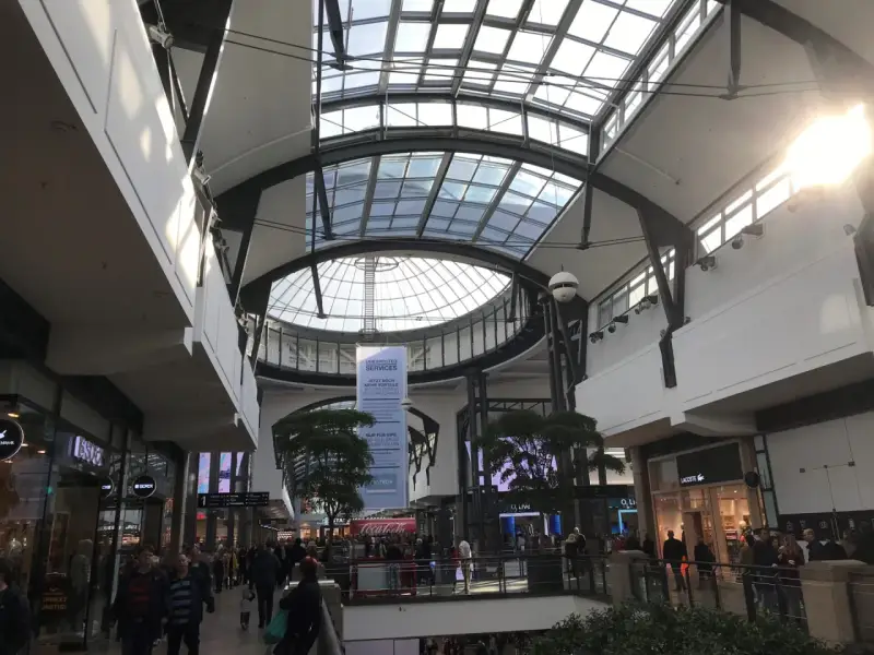 Helles, modernes Einkaufszentrum mit Glasdach. Menschen schlendern durch das Oberhausen Centro, vorbei an Geschäften wie Lacoste.